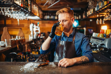 Male bartender tasting beverage at the bar counter