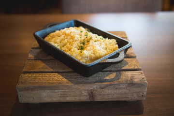 Mac n cheese presented n black oven dish on wooden block