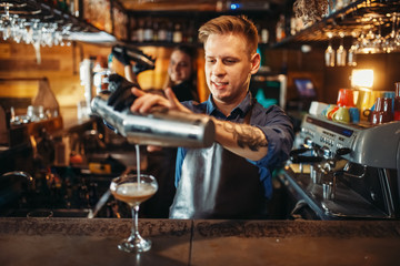 Male barman pouring the drink from the shaker