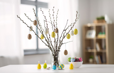 holidays and object concept - pussy willow branches decorated by easter eggs in vase and candles on...