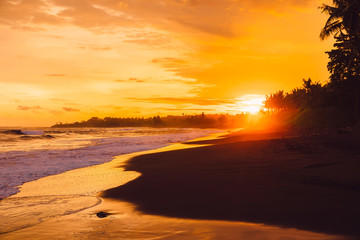 Warm sunset or sunrise with ocean waves and coconut palms in east coast of Bali