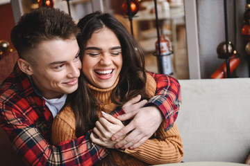 Cute young happy loving couple sitting in cafe indoors hugging.
