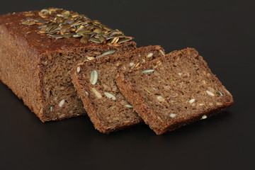 Home baked rye bread with sunflower seeds and cut off slices - close up on black background