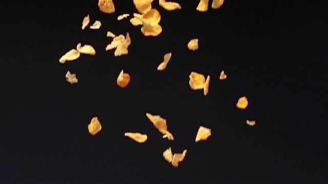 Crispy yellow corn flakes fall down to the ground on black background in Slow Motion