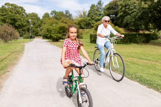 family, leisure and people concept - happy grandmother and granddaughter riding bicycles at summer park