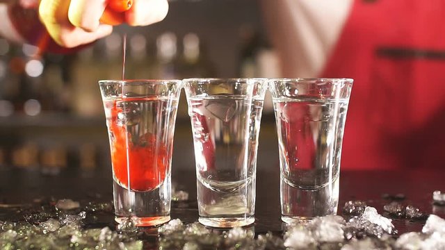 Bartender adding red drink into cocktail glass on the bar counter.