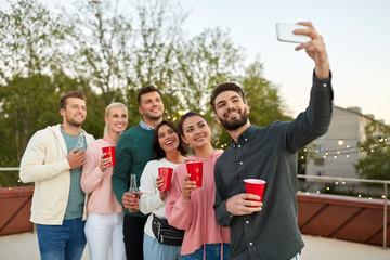 leisure and people concept - happy friends with non alcoholic drinks taking selfie by smartphone at rooftop party in summer