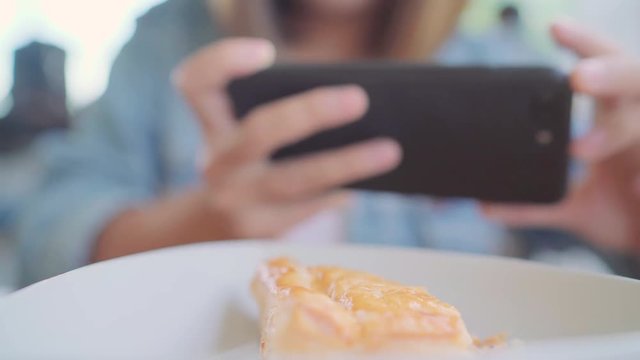 Food blogger Asian woman using phone for photo dessert, bread and drink while sitting on table in cafe. Lifestyle beautiful women relax at coffee shop concepts.