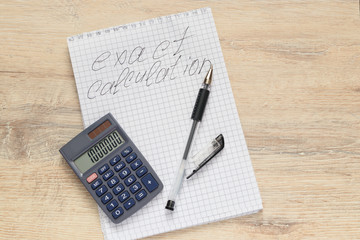 notepad  with the inscription Exact Calculation, with a open calculator  and pen on the table