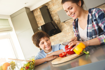 Family at home standing in kitchen together son looking at mother cutting vegetables joyful