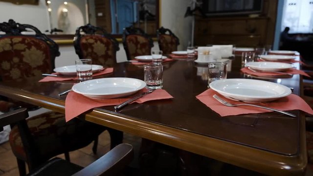Table setting in a prestigious restaurant. Deep plates and glass goblets, forks on a chic polished wooden table of a prestigious restaurant. Aristocratic decoration. Smooth camera movement
