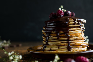 Stack of banana pancakes topped with chocolate drizzle and frozen raspberries