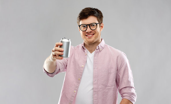 Drinks And People Concept - Happy Young Man In Glasses Drinking Soda From Tin Can Over Grey Background