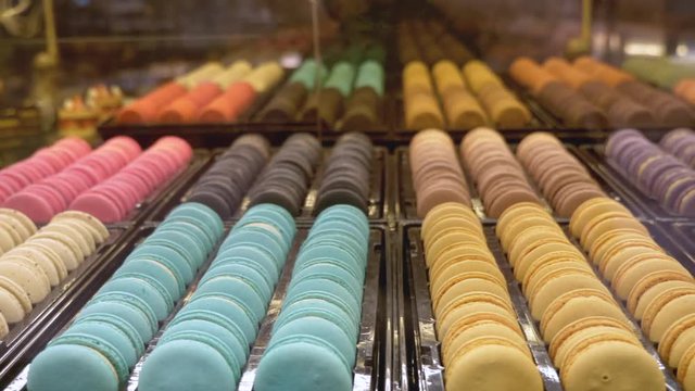 Rows of multicoloured macaroons set out on display, mirrored reflection in background as shot pan's across.