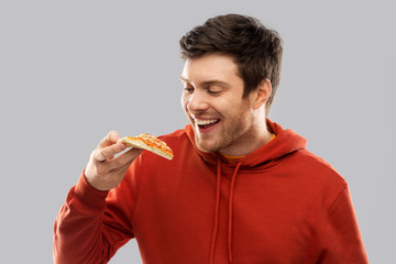 fast food and people concept - happy smiling young man in red hoodieeating pizza over grey...