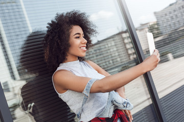 Young woman in the city street near window taking selfie on smartphone smiling cheerful side view close-up