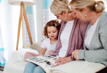 A small girl with mother and grandmother at home, looking at photographs.