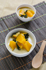 Delicious Thai dessert. Pumpkin in sweet coconut milk in white bowl on wooden table for served after lunch. 