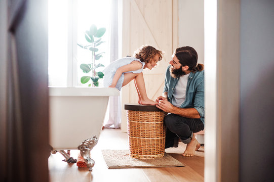 Young father painting small daugter's nails in a bathroom at home.