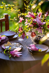 Beautiful table setting in garden on sunset light. Table decorated with magnolia flowers under magnolia tree.