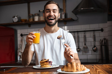 Image of attractive guy 30s eating food while having breakfast in modern apartment