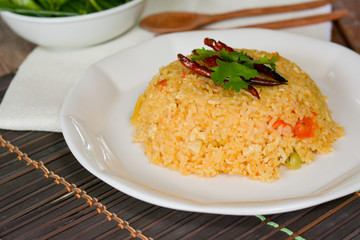 Tomato fried rice served with red dried chili in white dish on wooden table.  