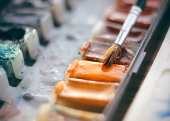 Watercolor paint in cuvettes of different colors-blue, orange and others and a brush for drawing with a large thick pile