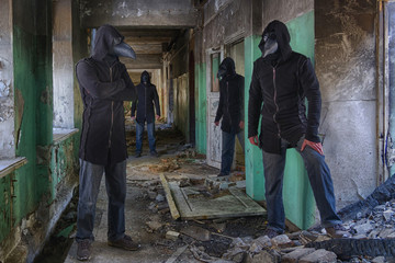 Four identical  mans in plague doctor masks, in hood and with a knife in an abandoned hospital or an insane asylum. Maybe picture for horror movie