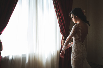young bride in white dress near window