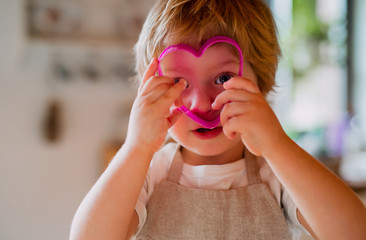 A small toddler boy looking through a cake cutter at home.
