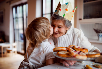 Senior grandmother with small toddler boy making cakes at home, kissing.