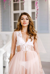 Cool girl in soft pink negligee poses in a spring studio