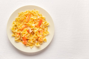 A photo of a plate of farfalle pasta with salmon and a cream sauce, shot from above on a white linen tablecloth with copyspace