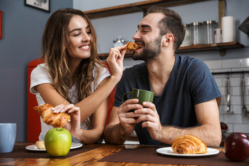 Portrait of european couple eating croissants while having breakfast in stylish kitchen