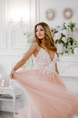 Lovely girl in a pink-white dress posing in a refined hall