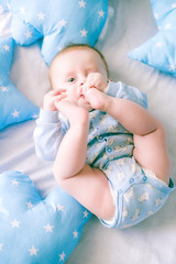 Cute toddler boy on bed at home surrounded by blue pillows