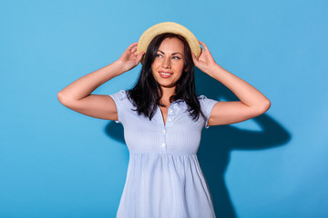 Freestyle. Woman in dress and hat standing isolated on blue wall looking aside dreamful