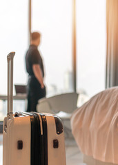 Luggage with blurred businessman in luxury hotel guest room looking out toward city view - obrazy, fototapety, plakaty