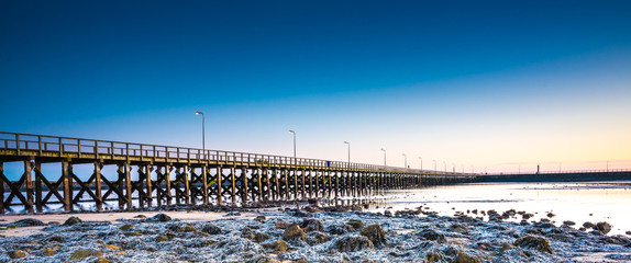 Wooden pier, clouds and stormy sky reflected in calm waters of North Sea - seaside landscape of...