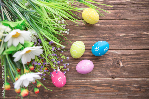 Easter eggs and spring flowers on rustic wooden background.