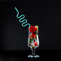 Coctail glass with plastic straw full of plastic and battery waste as imitation of real drink on square black background. Ecology concept of getting pollution to food and drinks