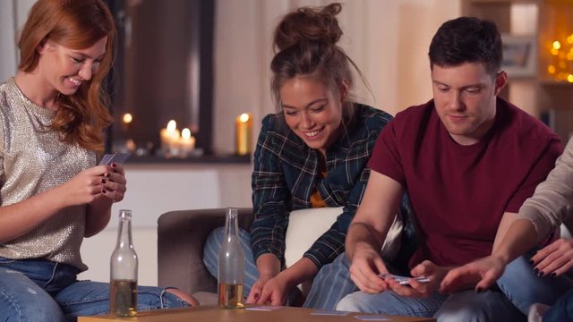 friendship, leisure and entertainment concept - happy friends playing cards game at home in evening