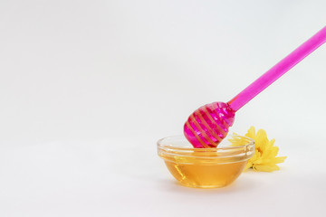 purple honey dipper takes honey from a bowl full of honey on a white background.