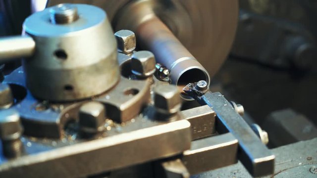 A metal part rotates and sharpeners on the lathe in the workshop in the manufacturing. Close-up.