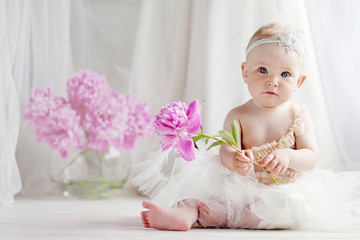 Little pretty girl with blue eyes sits on a floor with flowers of a peony. Copy space
