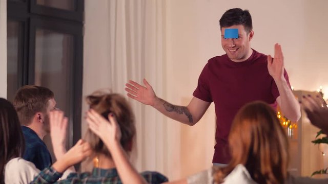 friendship, leisure and entertainment concept - happy friends playing guessing game at home in evening