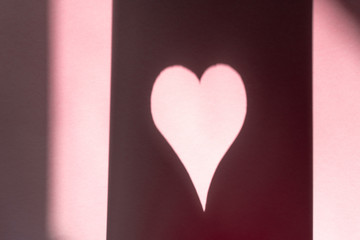 Background with a pink sheet of paper with a heart made of shadow and light
