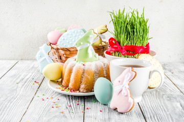 Easter table setting concept, festive table with decoration of young grass, cake, pastel colored eggs, homemade cookies in shape of eggs, bunny rabbits. On a wooden background, copy space