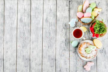 Easter table setting concept, festive table with decoration of young grass, cake, pastel colored eggs, homemade cookies in shape of eggs, bunny rabbits. On a wooden background, copy space