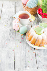 Easter table setting concept, festive table with decoration of young grass, cake, pastel colored eggs, homemade cookies in shape of eggs, bunny rabbits. On a wooden background, copy space